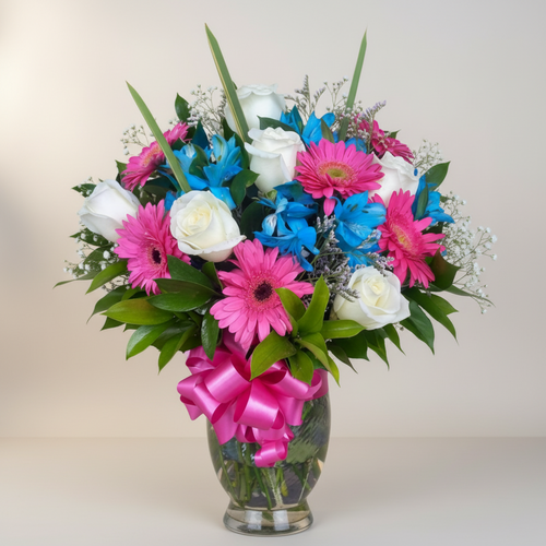 Arreglo floral en jarrón de cristal con flores rosas, azules y blancas