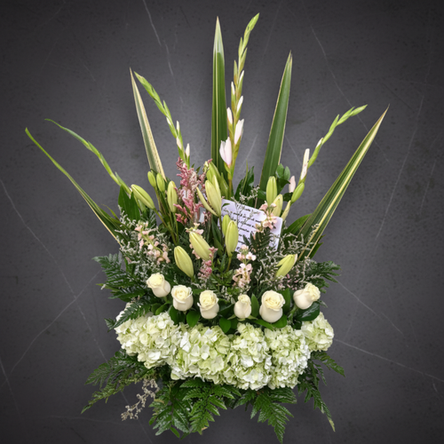 Arreglo floral vertical con flores blancas y verdes sobre fondo gris oscuro