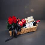 Arreglo ANGELO: Elegante cesta de mimbre con rosas rojas frescas, manzanas rojas, botella de vino tinto Finca Las Moras y caj