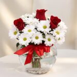 Arreglo floral Antonietta con rosas rojas, margaritas blancas y lazo rojo en jarrón de cristal, ideal para regalar en ocasion