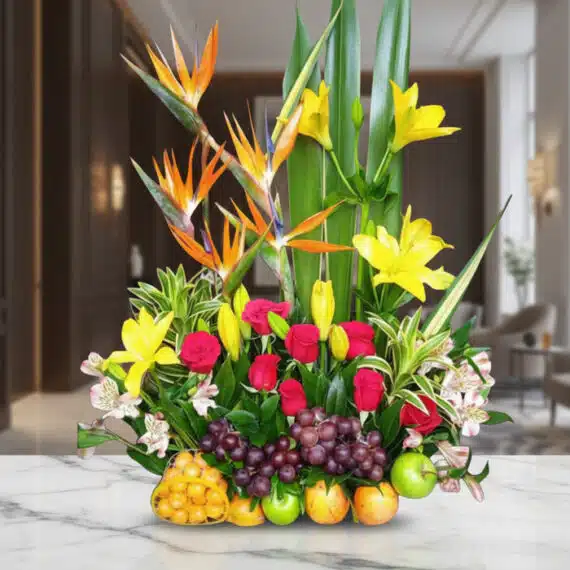 Arreglo Floral con Frutas Akebia: Elegancia y Frescura para tu Hogar Arreglo floral Akebia con aves del paraíso, lirios amarillos, rosas rojas, uvas y manzanas verdes sobre mármol blanco en un l