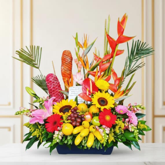 Arreglo floral exótico con heliconias, girasoles, lirios, anturios y frutas tropicales como plátanos, uvas, manzanas y limone