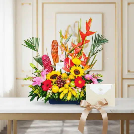 Arreglo floral exótico con heliconias, girasoles, lirios y frutas tropicales, acompañado de una tarjeta de regalo y cinta sat