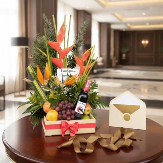 Arreglo floral exótico con flores de ave del paraíso y heliconias, piñas, uvas, manzanas y naranjas, acompañado de una botell