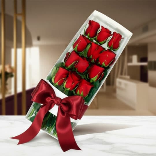 Caja de 12 rosas rojas frescas y vibrantes, presentadas en un elegante estuche blanco con un lazo de satén rojo, sobre una su