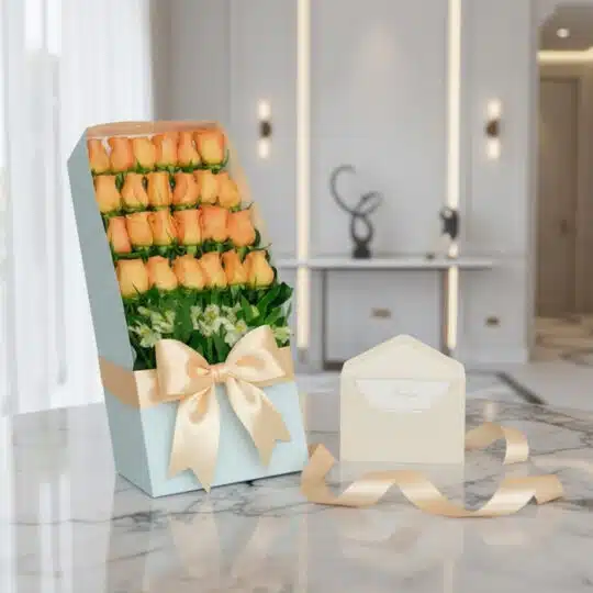 Caja de 24 rosas salmón frescas en empaque azul con lazo satinado, tarjeta de regalo y cinta sobre mármol.