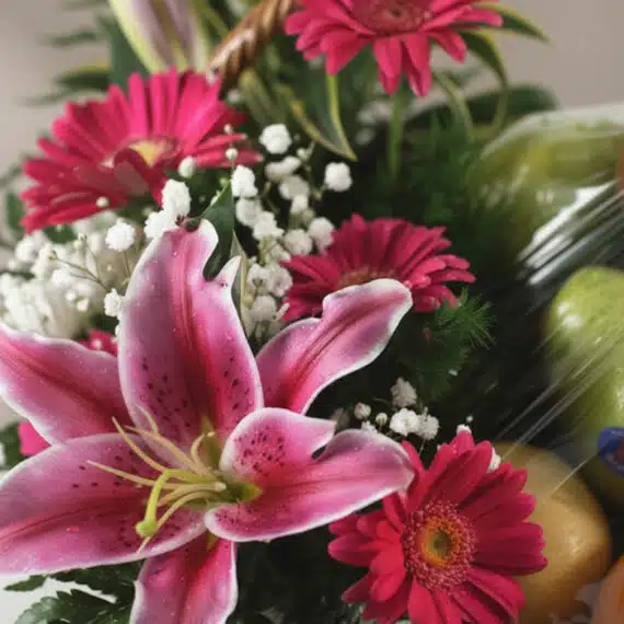 Primer plano extremo de la Canasta Frutal CARMINE con lirios rosados, gerberas fucsia, gypsophila blanca y frutas frescas, de
