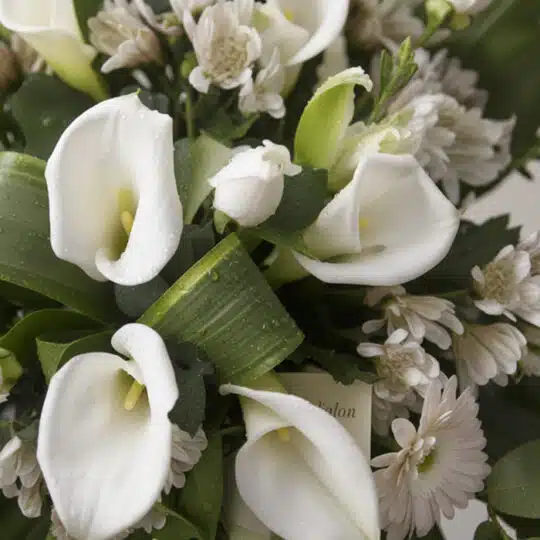 Fotografía macro premium de la Corona Fúnebre 'Homenaje Guadalupe', mostrando calas blancas, rosas y crisantemos con rocío, c