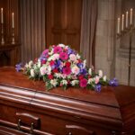 Cubre caja fúnebre "El Legado de Francisco" con flores variadas en tonos rosas, morados y blancos, sobre un ataúd de madera o