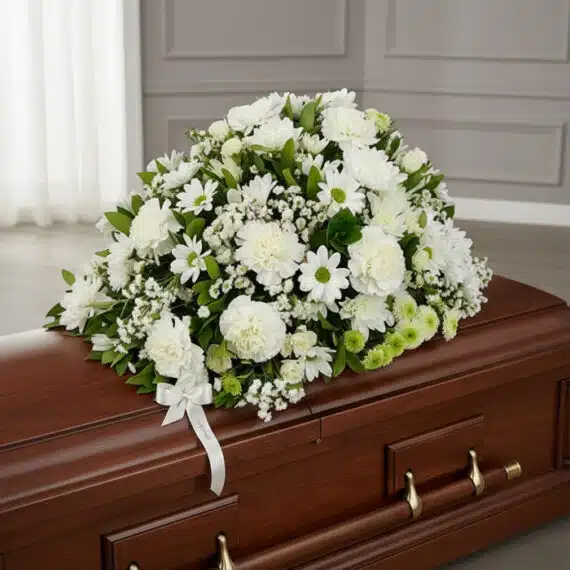 Cubre caja fúnebre Epifania con flores blancas y cinta de condolencia, vista desde un ángulo diferente y composición renovada