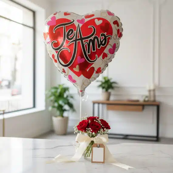 Globo metalizado en forma de corazón con la frase 'Te Amo' flotando sobre un arreglo de rosas rojas frescas en un jarrón de c