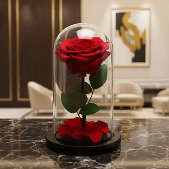 Rosa preservada roja en cúpula de cristal sobre una mesa de mármol negro, con un fondo elegante de lobby de hotel boutique.